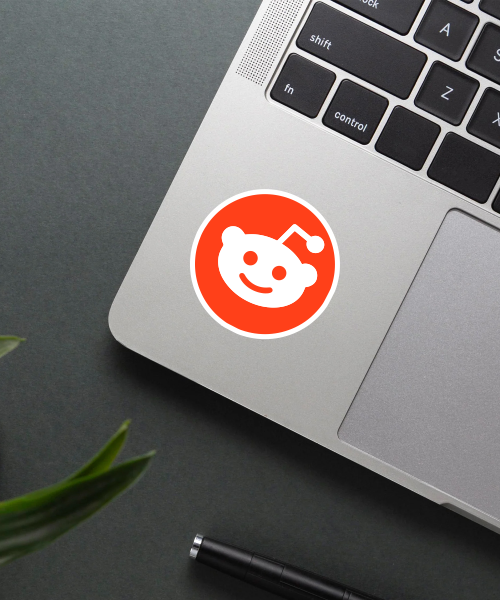 reddit logo sticker on laptop surface showing bright orange circle and white alien face