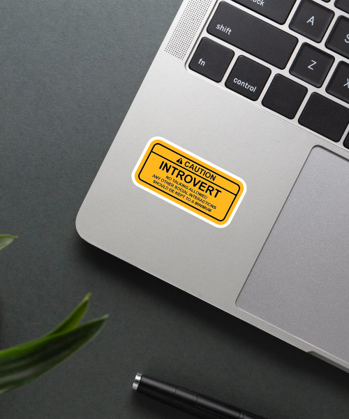 caution introvert sticker on laptop surface showing yellow and black caution style design
