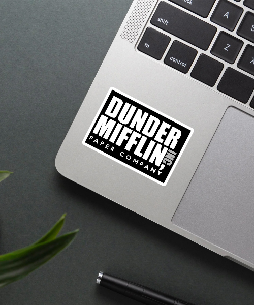 dunder mifflin sticker on laptop surface showing bold black and white logo